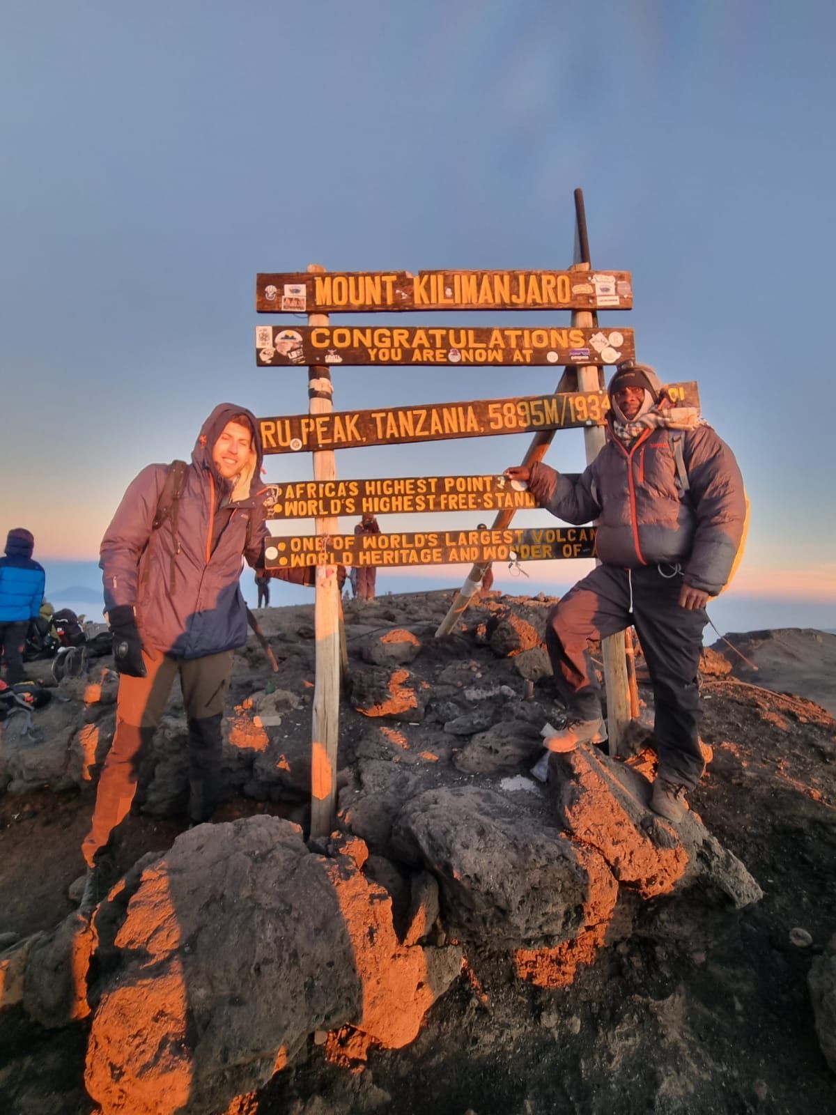 Ein Bergsteiger und sein Guide am Schild des Uhuru Peak bei Sonnenaufgang